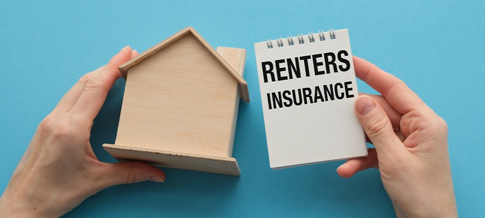 A hand holding a house and a piece of paper that says Renters Insurance. The image conveys the importance of renters insurance for protecting one's belongings in case of damage or loss