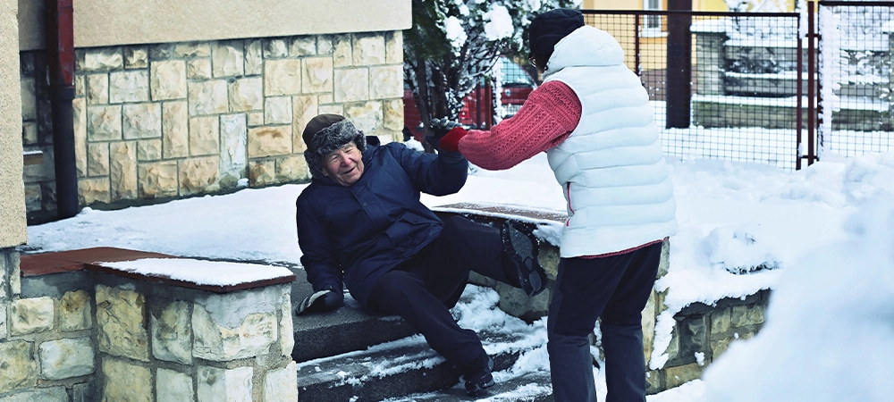 Senior man falling down from the slippery, icy and snowy stairs in front of a house. His wife is trying to help him. Prevention of safety to injure old people before slipping accident on the stairs.