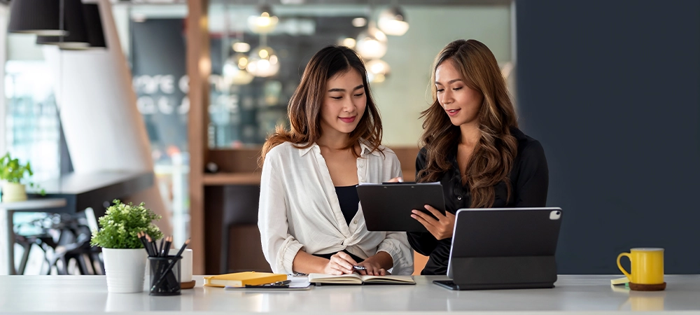 Two young Asian business woman talk, consult, discuss working with new startup project idea presentation analyze plan marketing and investment in the office.